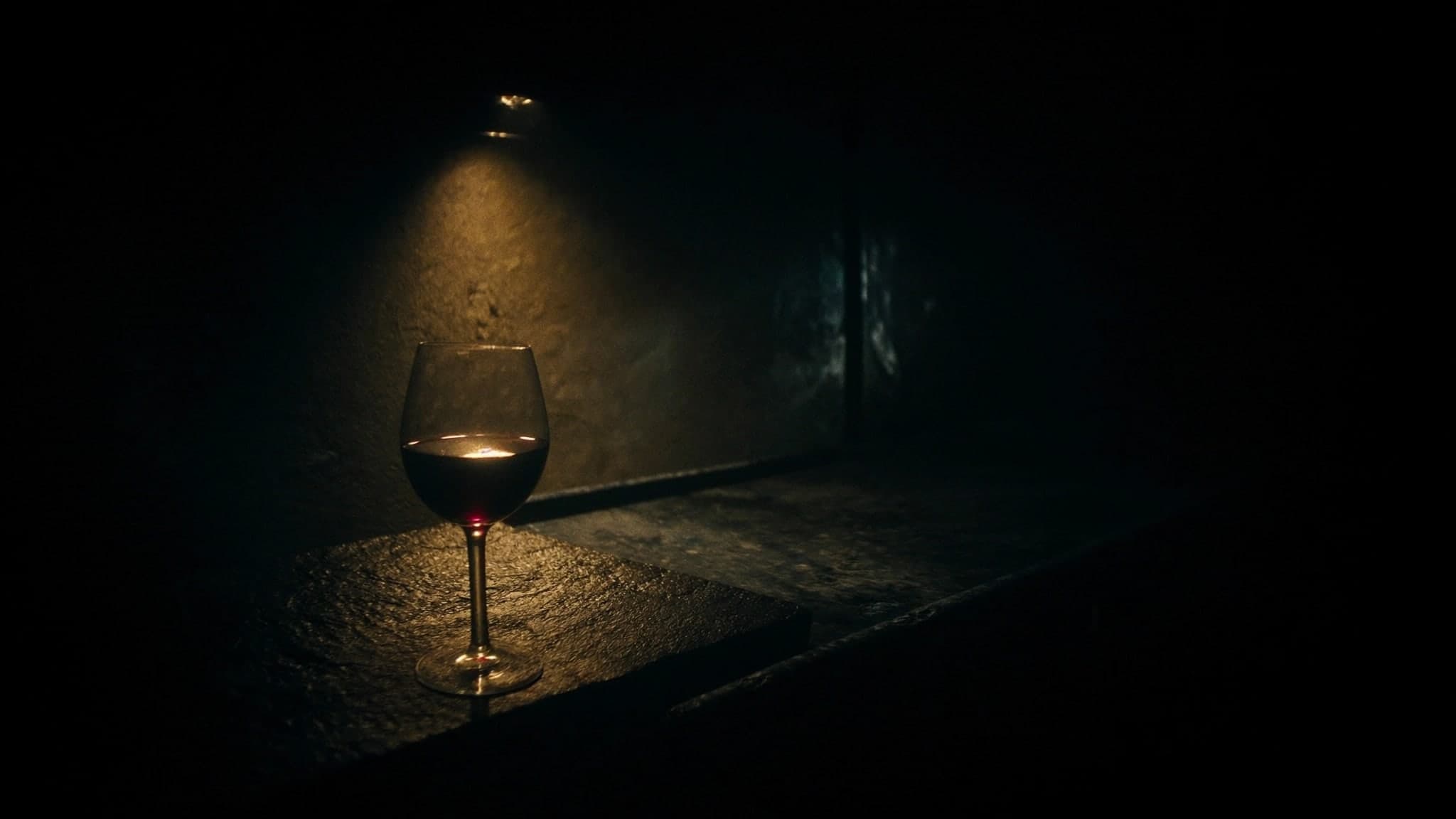 Un calice di vino rosso su pietra, illuminato da un fascio di luce